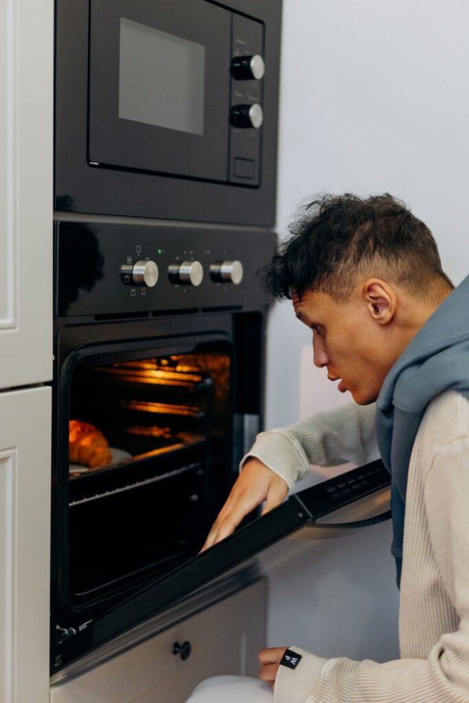 A man checking baked items in an oven, capturing a moment in a modern kitchen setting.